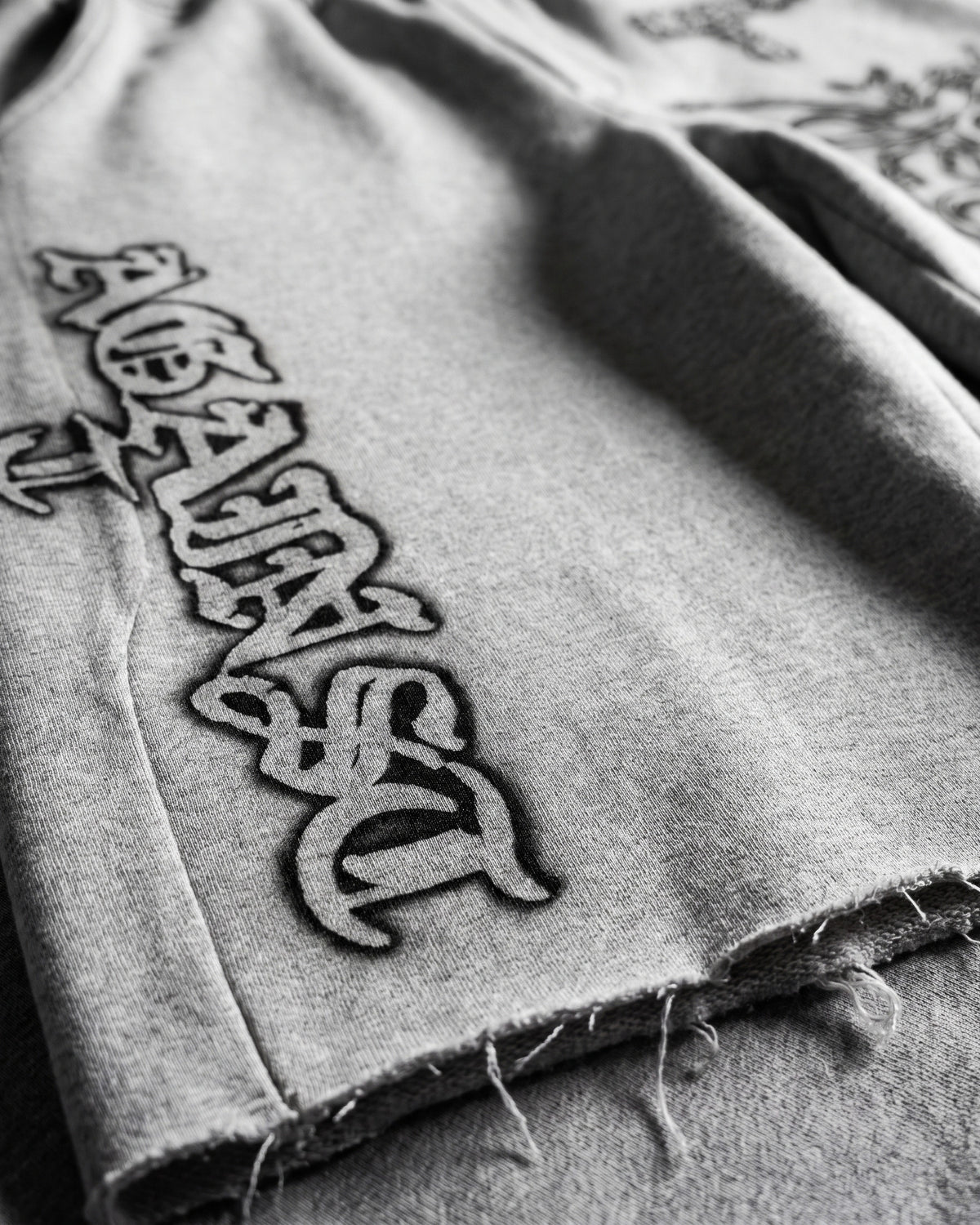 ATO GREY AIRBRUSH SWEAT JORTS – close-up of the gothic "Against" side lettering and raw-cut hem