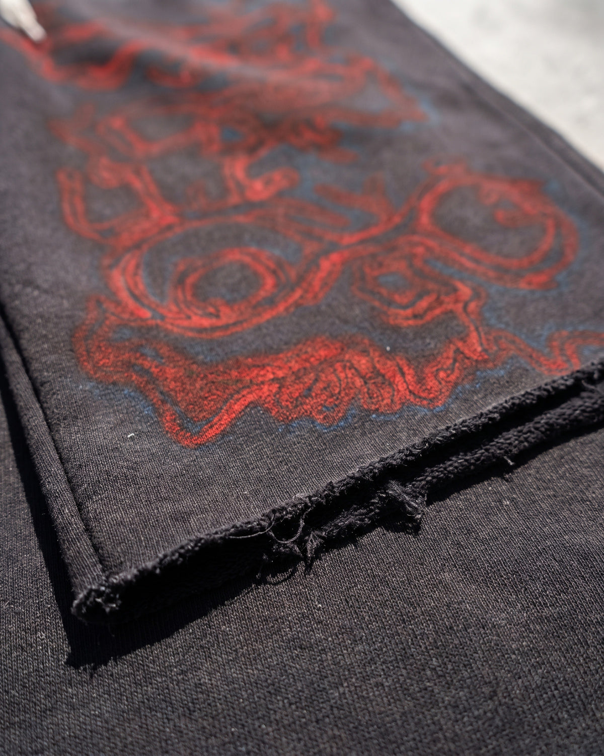 ATO BLACK AIRBRUSH SWEAT JORTS – close-up of the raw-cut hem and red airbrush